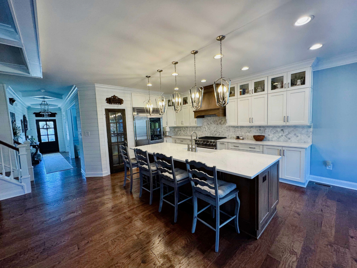 Spacious kitchen with white cabinets and marble countertops, featuring a large island with blue chairs and pendant lighting. 