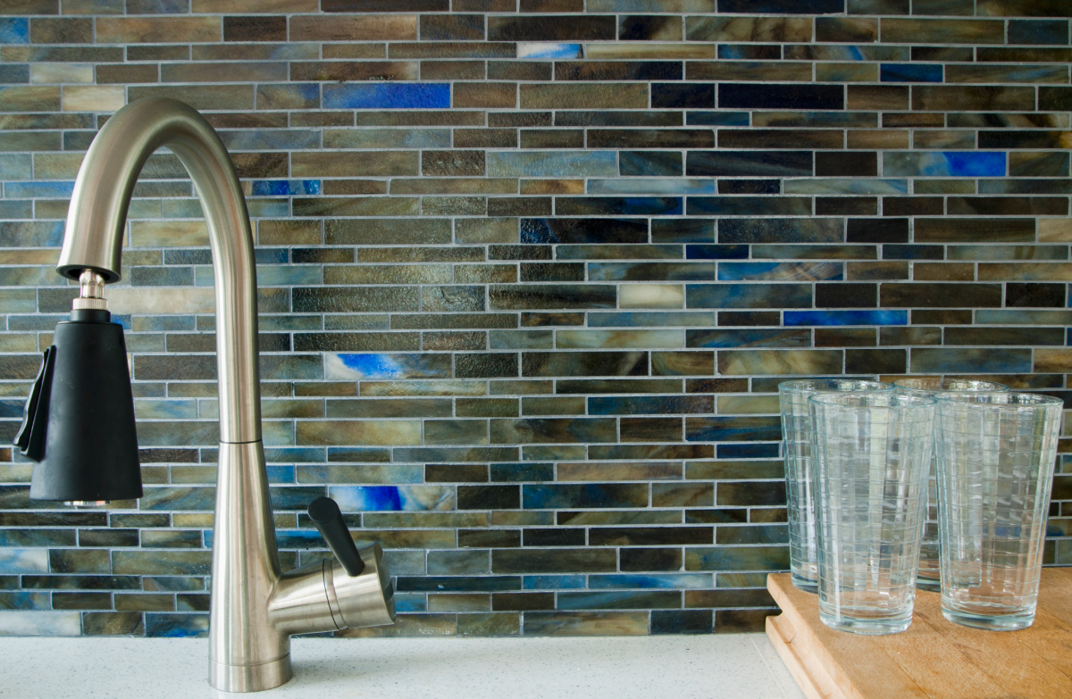 Kitchen sink with modern faucet against a backsplash of multicolored rectangular tiles, featuring blue accents. 