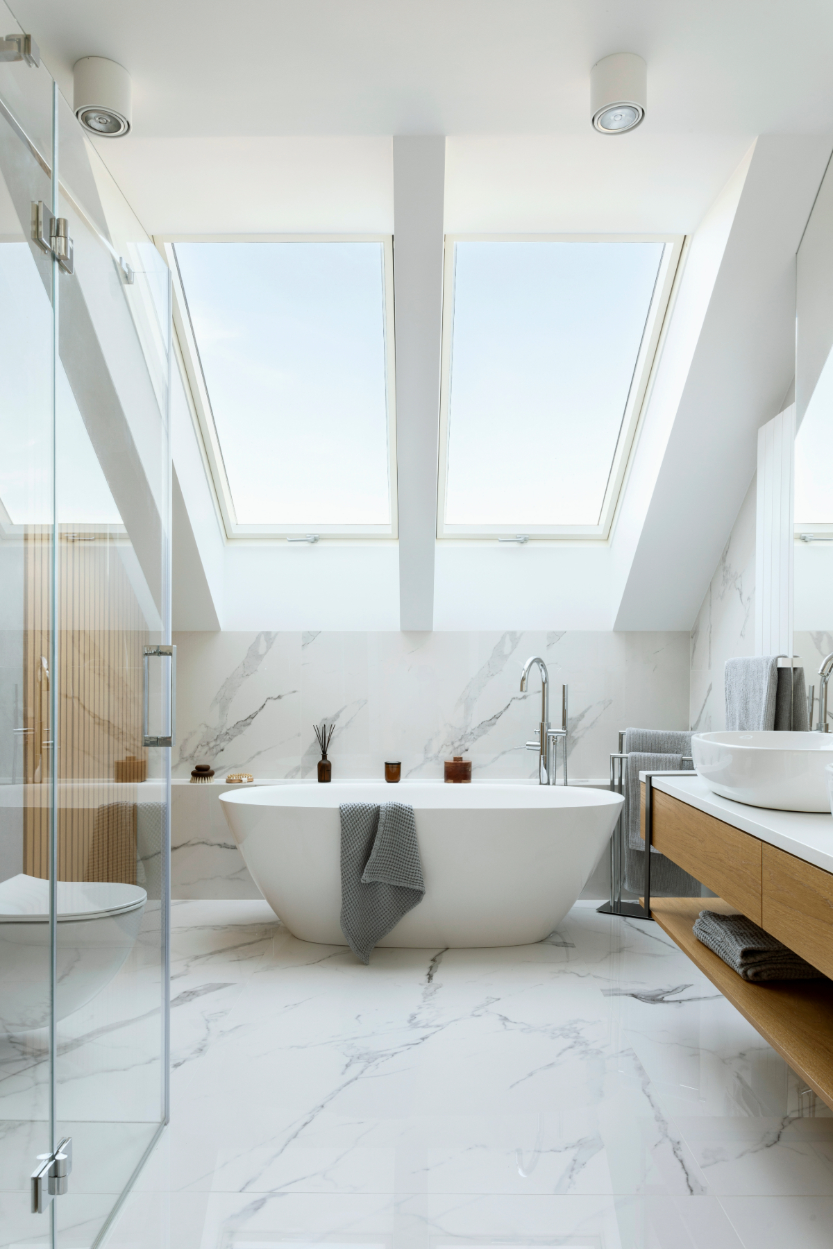 Bright and airy modern bathroom with white marble design, freestanding tub, and skylights. 