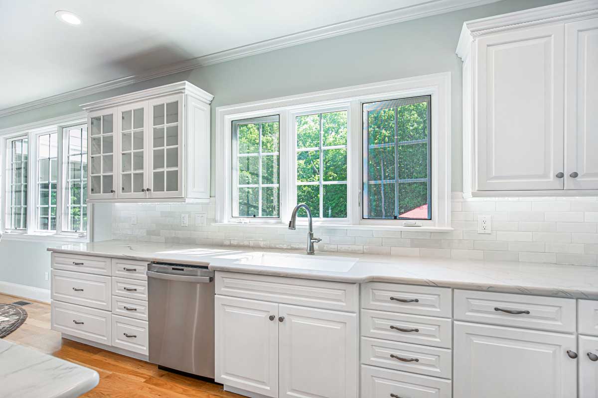 Bright kitchen with white cabinetry and subway tile backsplash, featuring large windows overlooking greenery. 